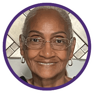 Portrait of a smiling person with glasses and earrings in front of a decorative background.