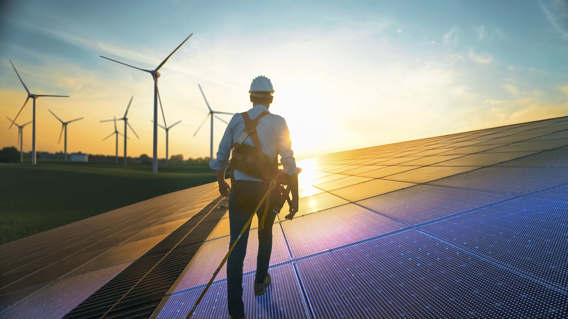 Professional Male Green Energy Engineer Walking On Solar Panel, Wearing Safety Belt And Hard Hat. Man Inspecting Sustainable Energy Farm With Wind Turbines. VFX Edit Visualizing Electricity Flow.